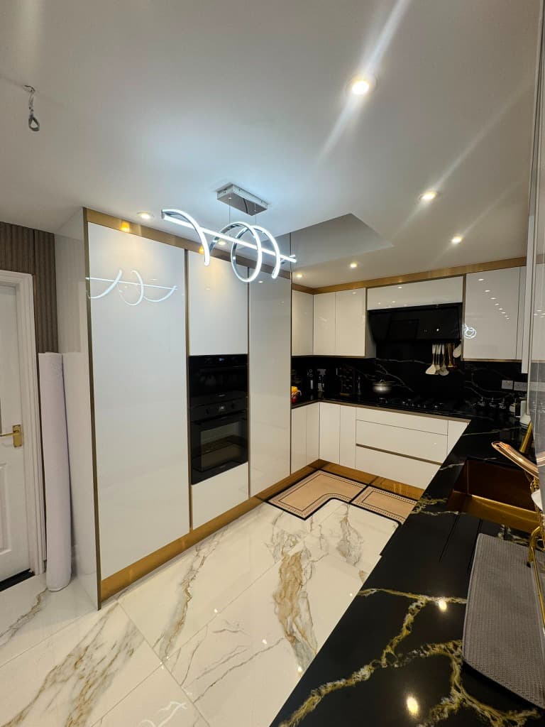 Luxurious white gloss kitchen with gold profiles and dark marble worktops